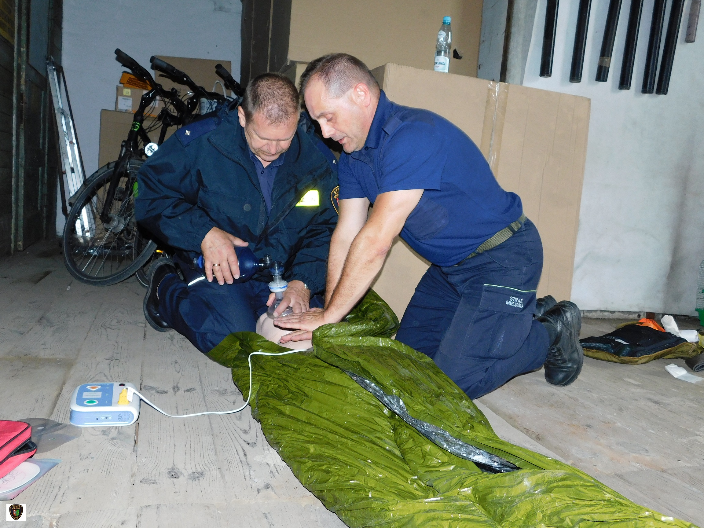 Zdjęcie przedstawia dwóch strażników miejskich wykonujących wspólnie na manekinie resuscytację krążeniowo-oddechową z wykorzystaniem AED 