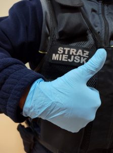 Zdjęcie przedstawia rękę strażnika miejskiego w rękawiczce ochronnej z uniesionym kciukiem na znak OK