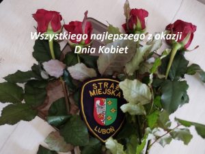 Zdjęcie przedstawia czerwone róże oraz znak identyfikacyjny Straży Miejskiej Miasta Luboń