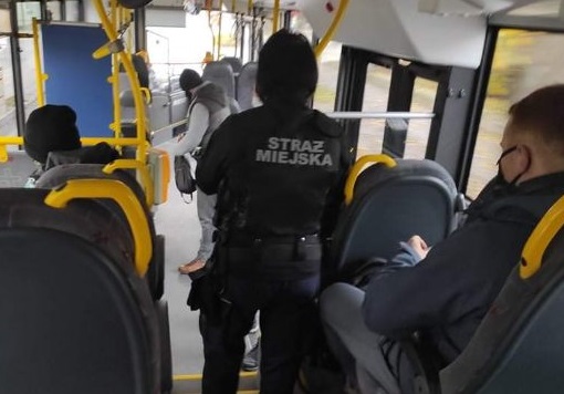 Zdjęcie przedstawia funkcjonariusza straży miejskiej podczas kontroli w autobusie