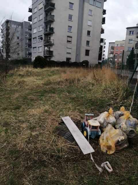 Zdjęcie przedstawia worki ze śmieciami na terenie zielonym przy blokach mieszkalnych