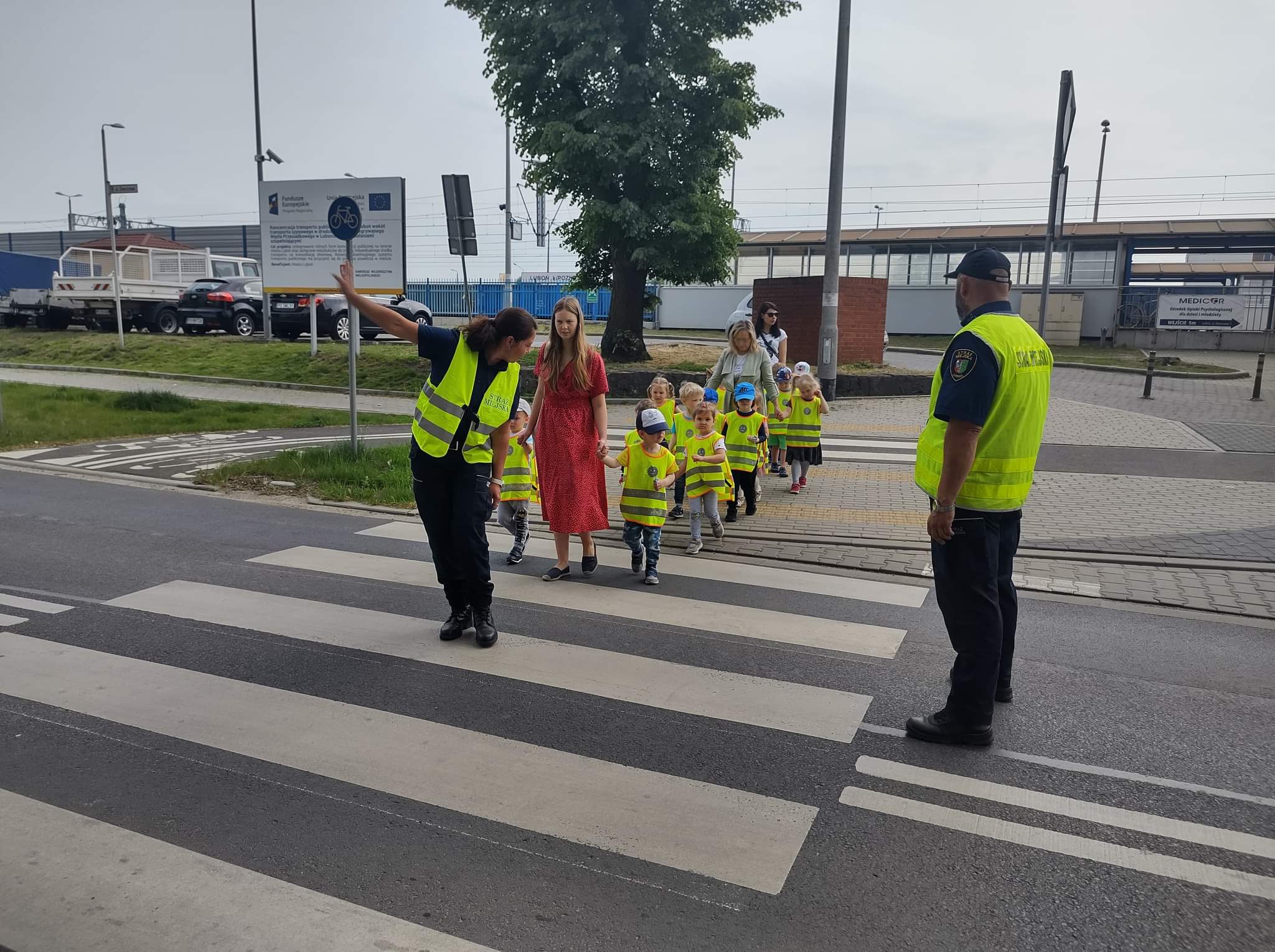 Zdjęcie przedstawia przedszkolaki oraz strażników miejskich na przejściu dla pieszych