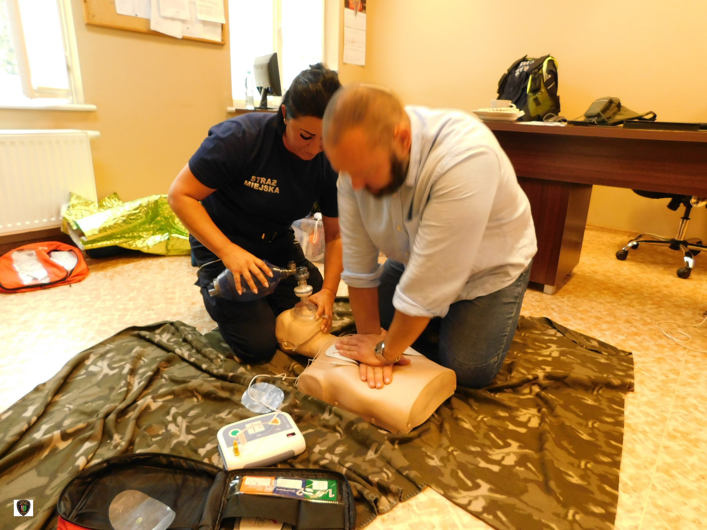 zdjęcie przedstawia strażniczkę i strażnika miejskiego, wykonujących wspólnie na manekinie resuscytację krążeniowo-oddechową z wykorzystaniem AED