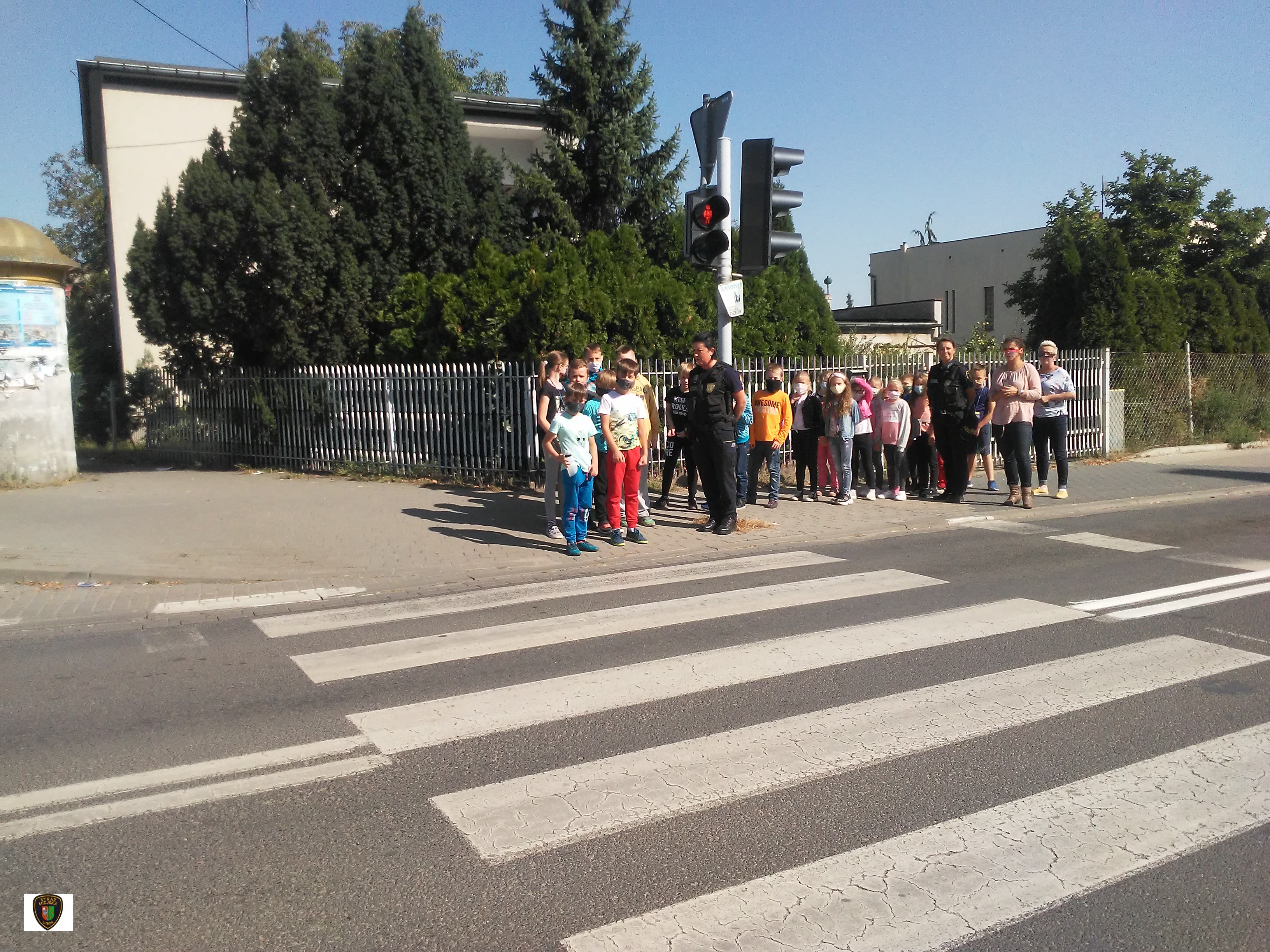 zdjęcie przedstawia dzieci stojące przed przejściem dla pieszych w obecności strażników miejskich