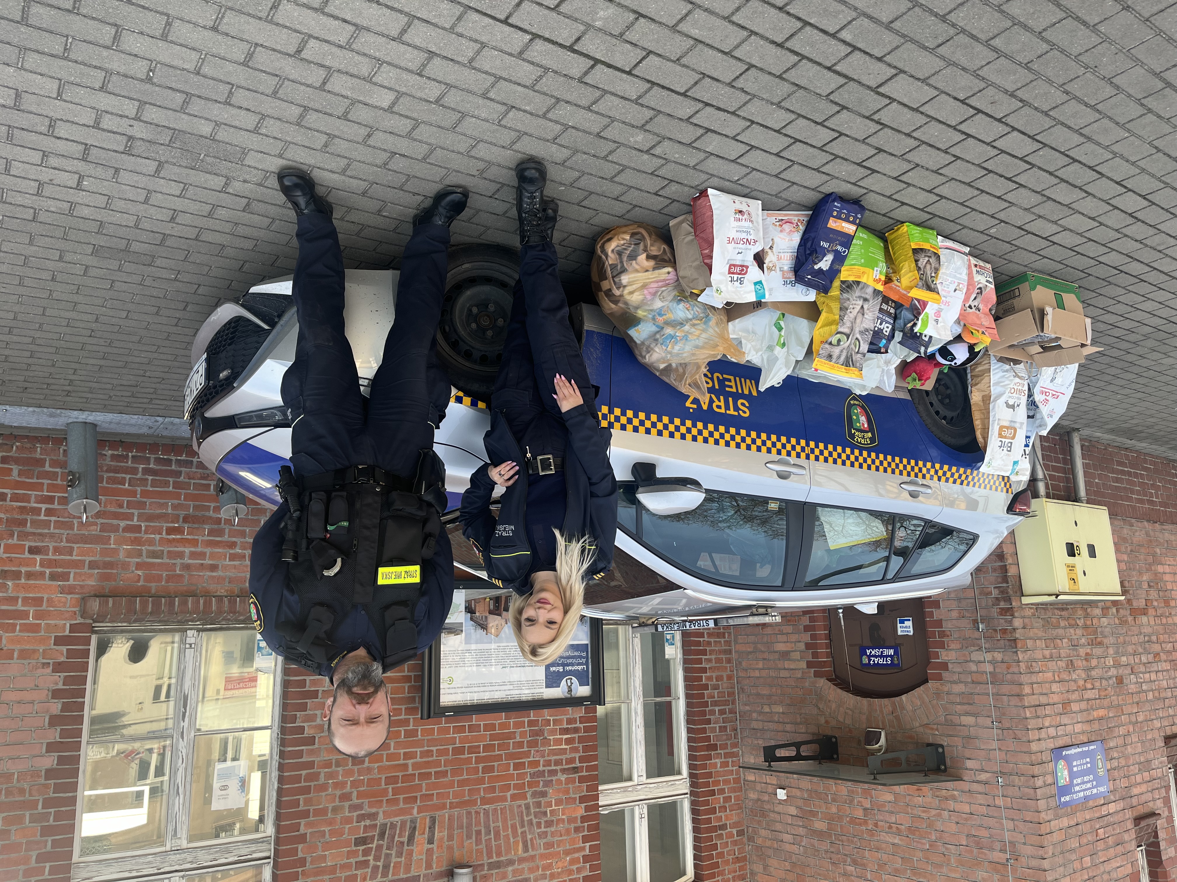 Zdjęcie przedstawia strażników miejskich oraz radiowóz z darami zebranymi dla Wielkopolskiego Inspektoratu Ochrony Zwierząt